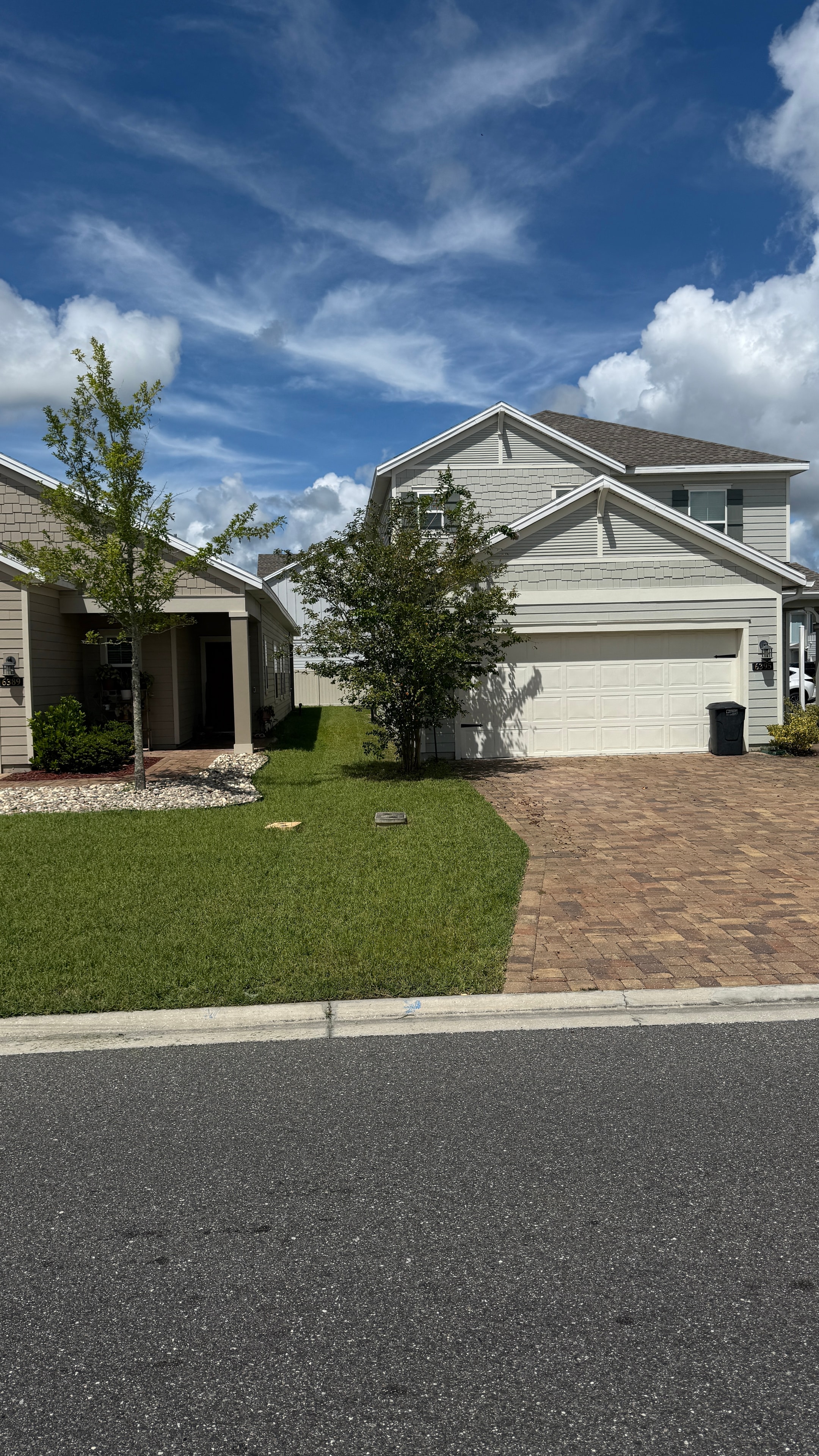 Two-story home with paver driveway and trimmed lawn