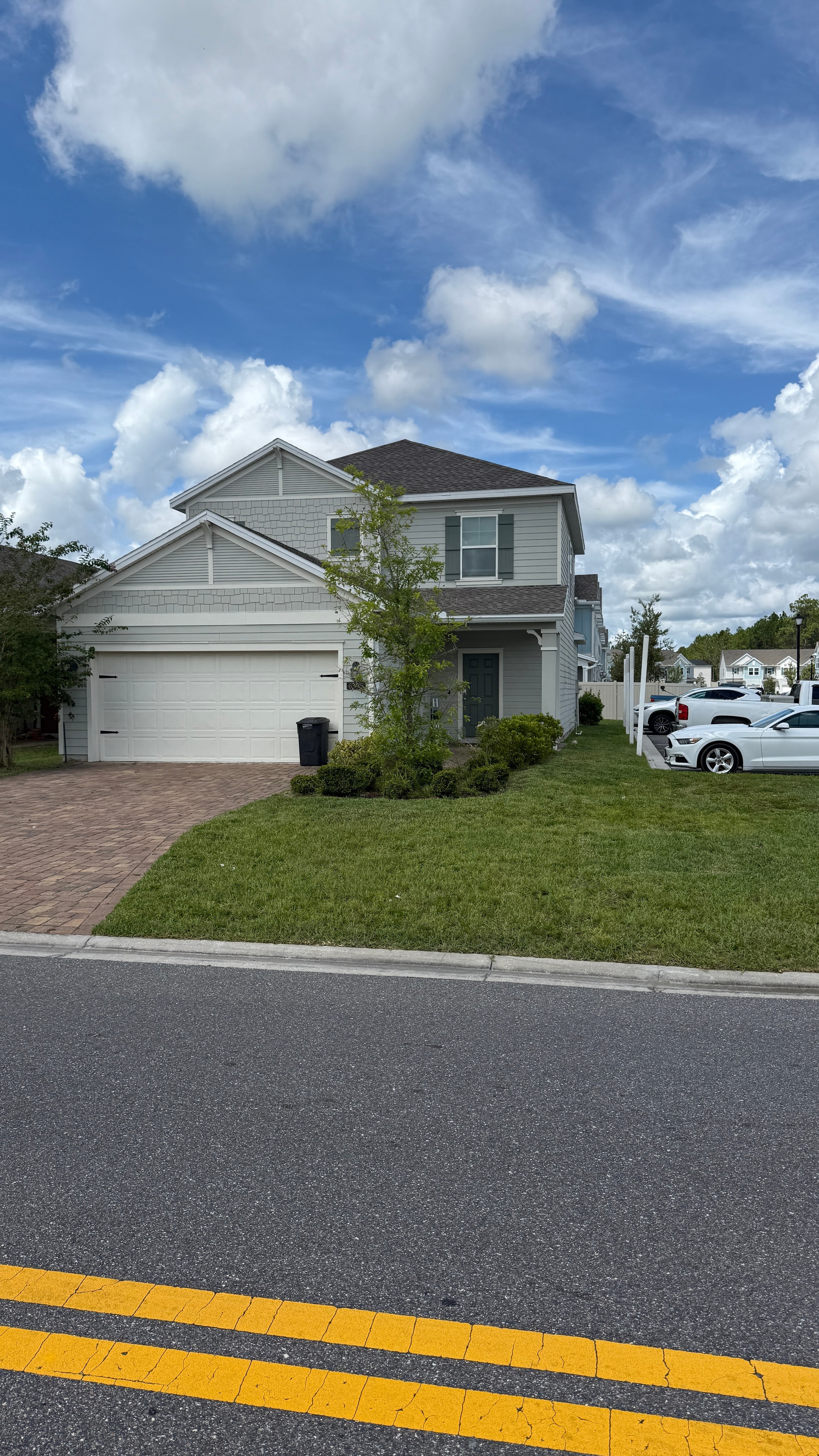 White two-story home with paver driveway and manicured lawn